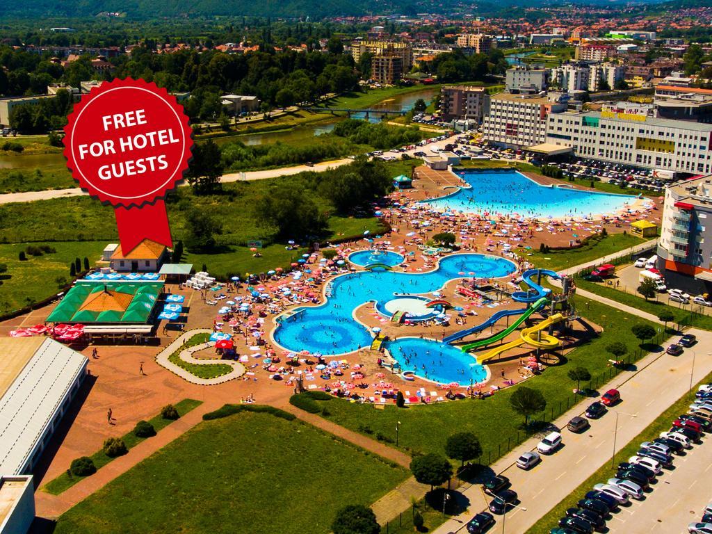 Hotel Hills Sarajevo Congress & Thermal Spa Resort Ilidža Εξωτερικό φωτογραφία The photo shows an aerial view of a large swimming pool area, likely part of a hotel or resort. There are several pools of different shapes and sizes, including one that resembles a Mickey Mouse shape. The area is filled with numerous sun loungers an